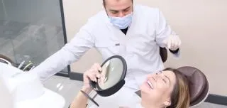 Female patient smiling in mirror while dentist evaluates results after anterior open-bite correction treatment.