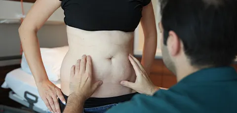 Doctor examining a woman’s lower abdomen during apron belly consultation in a Turkish clinic.