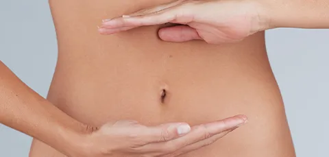 Close-up of female abdomen with hands framing the navel—illustrating belly button revision after tummy-tuck surgery.