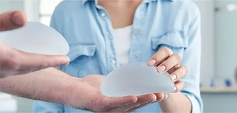 Patient holding silicone breast implants during consultation about breast implant replacement surgery