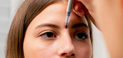 A doctor’s hands measuring a womans eyebrows in preparation for brow bone reduction surgery
