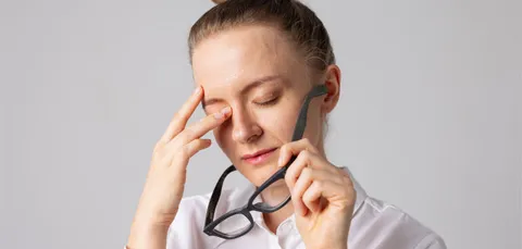 A woman holds her glasses and rubs her eye, experiencing eye strain and vision problems that can be caused by cataracts