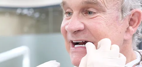 Older male patient smiling during dental implant check after treatment
