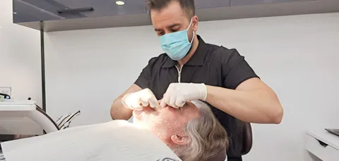 Dentist performing dental implant procedure on an older male patient in clinic