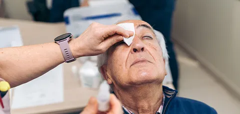 Elderly man receiving eye drops after cataract surgery, illustrating treatment and recovery from postoperative dry eye.  
