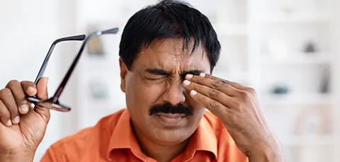 Man rubbing eyes in discomfort after removing glasses, showing link between dry eyes, headaches, and migraine pain.  