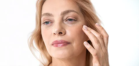 Close-up of mature woman touching skin around eyes with visible eyelid wrinkles before treatment in Turkey