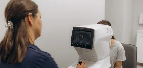 Technician operating femtosecond-laser eye scanner on patient before laser-assisted cataract surgery.