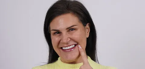 Smiling woman pointing at her teeth after dental treatment, showing satisfaction with results