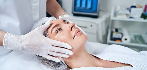 Clinician positioning middle-aged woman’s face before high-intensity focused ultrasound (HIFU) non-surgical facelift treatment