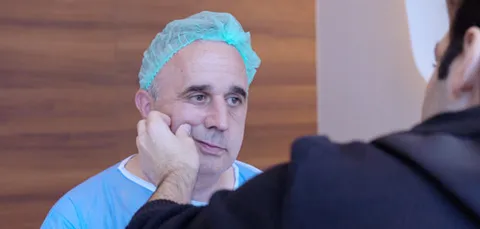 Surgeon examining male patients cheek during pre-op consult for buccal fat removal