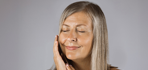 Smiling mature woman touching face after secondary facelift surgery in Turkey