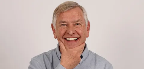 Happy senior man smiling and touching chin after full mouth dental implant restoration