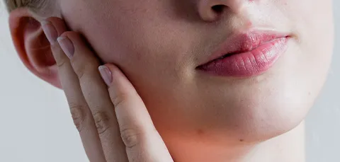 Close-up of woman touching jaw, showing discomfort before temporomandibular joint surgery in Turkey