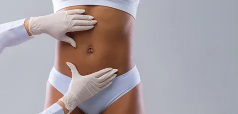 Gloved surgeon assessing woman’s abdomen before tumescent liposuction, highlighting differences from traditional liposuction