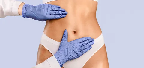 Surgeon in blue gloves palpating woman’s abdomen during pre-op assessment for VASER liposuction treatment